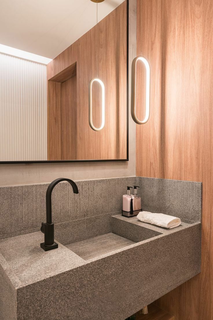 Lavabo com cuba esculpida em granito Cinza Andorinha, torneira preta, painel de madeira e espelho com luz embutida
