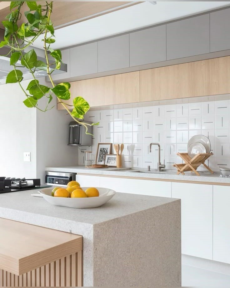 Cozinha clara com bancada e ilha em granito Itaúnas, revestimento branco na parede, cooktop e fruteira com laranjas