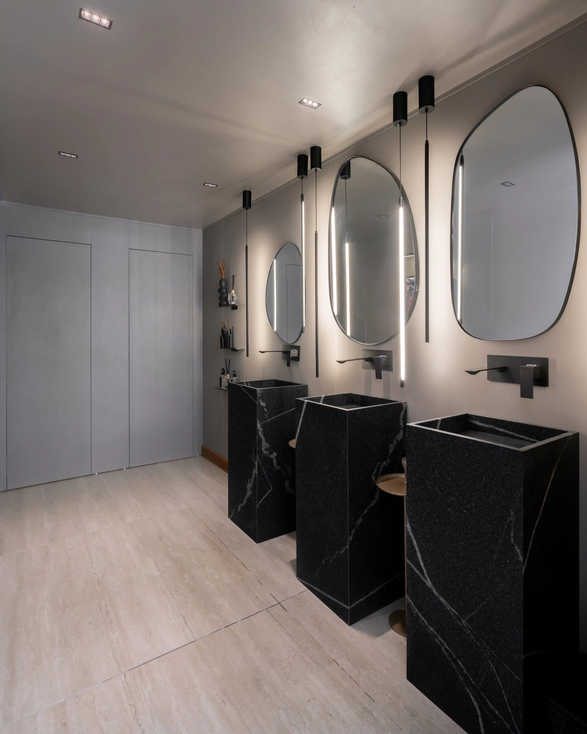 Banheiro com três cubas de pedestal esculpidas em granito Vincent Black, espelhos orgânicos com luz embutida e piso claro