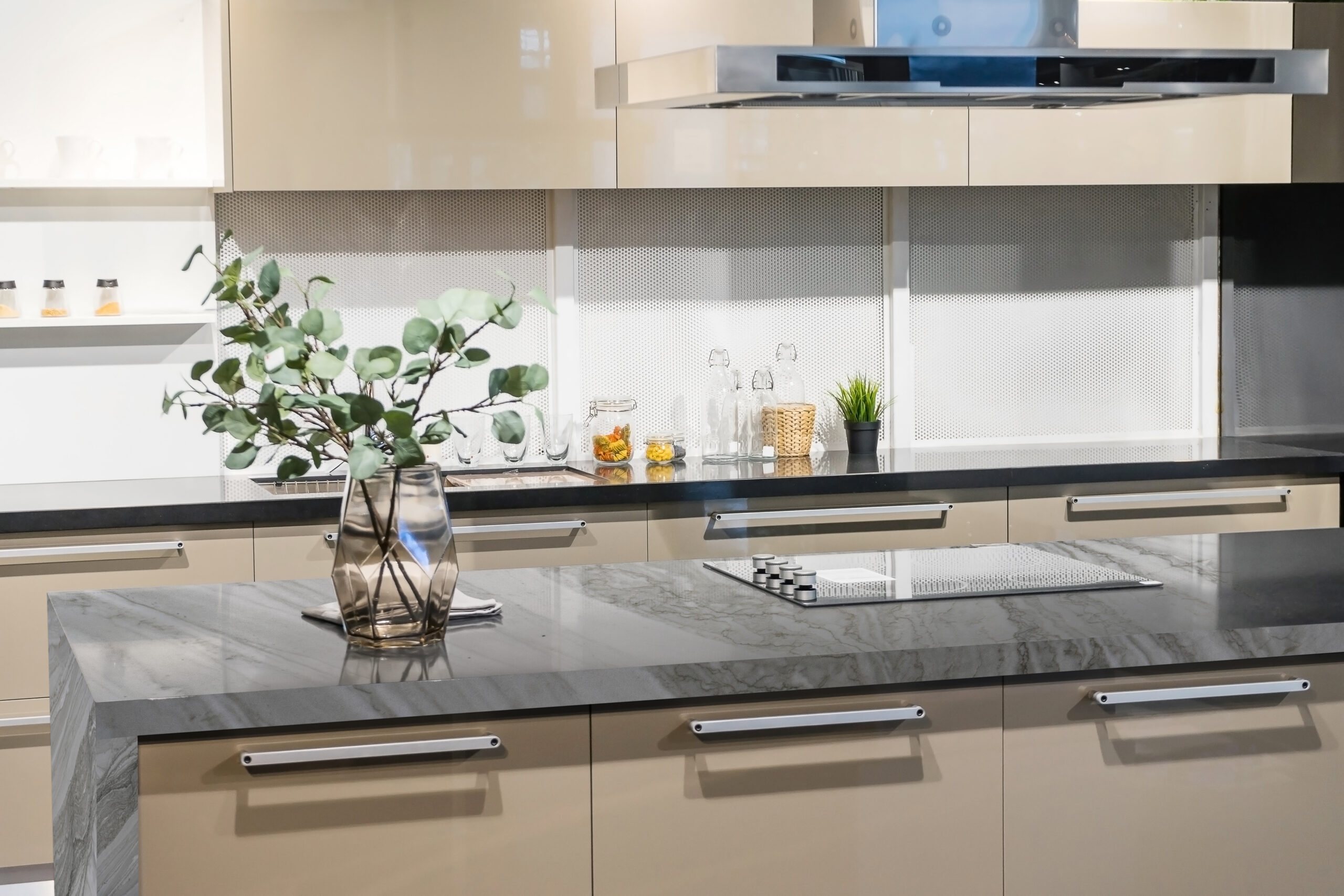 Cozinha com ilha em quartzito Polaris Verde, cinza com veios, cooktop embutido, vaso com eucalipto e armários bege