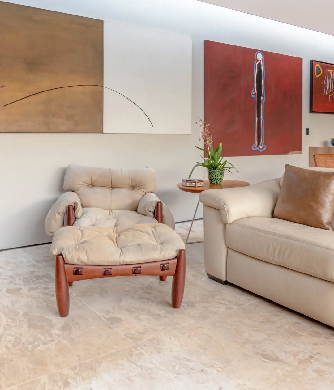 Sala de estar com piso de travertino Bege Bahia em placas grandes, poltrona de couro claro, sofá bege e quadros nas paredes